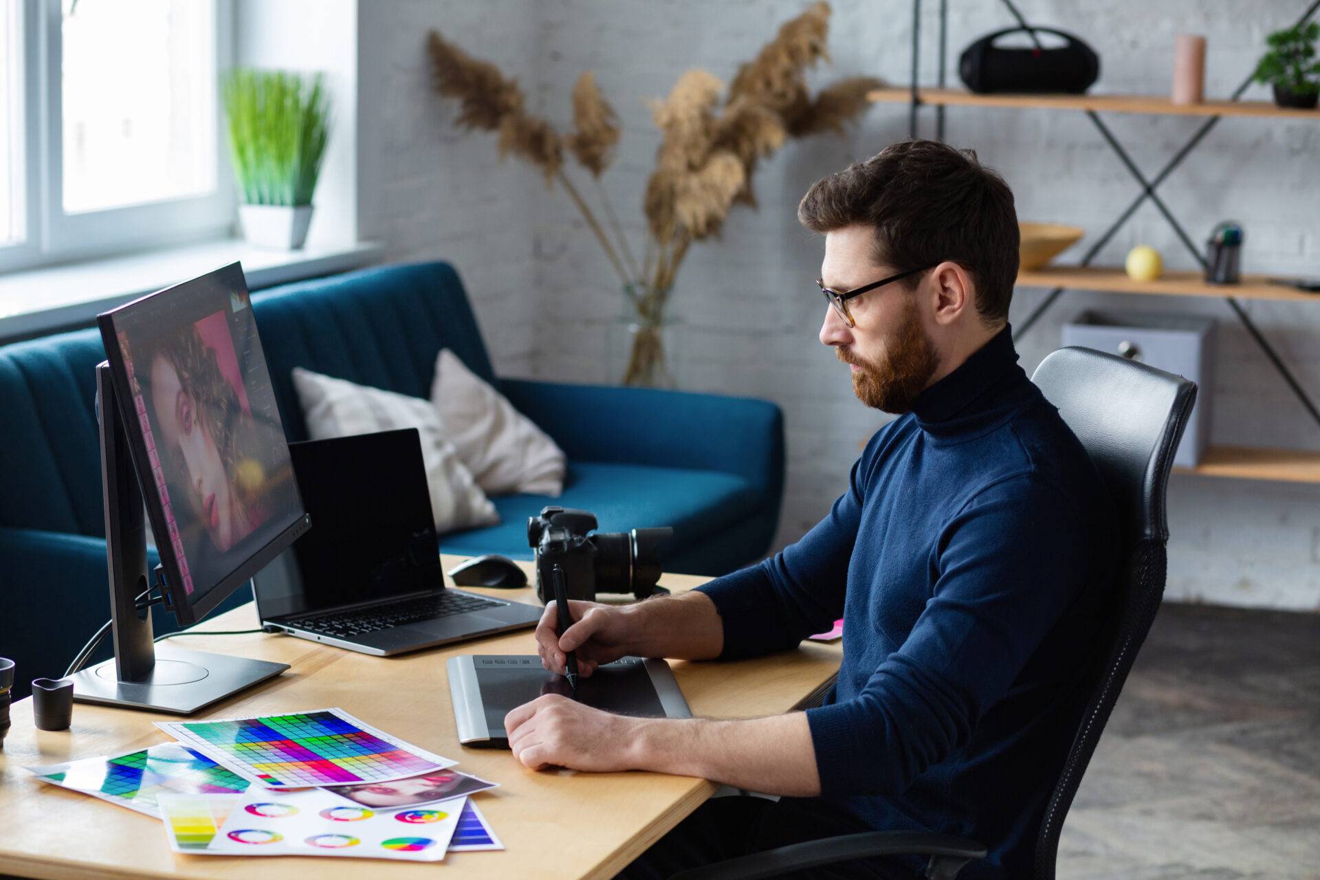 Photographer editing portraits on computer with color swatches and camera on desk in modern studio.