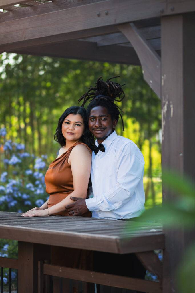 Couple posing for a portrait under a wooden gazebo with lush greenery in the background, showcasing professional photography by JCenteno Photography in Tampa, FL.