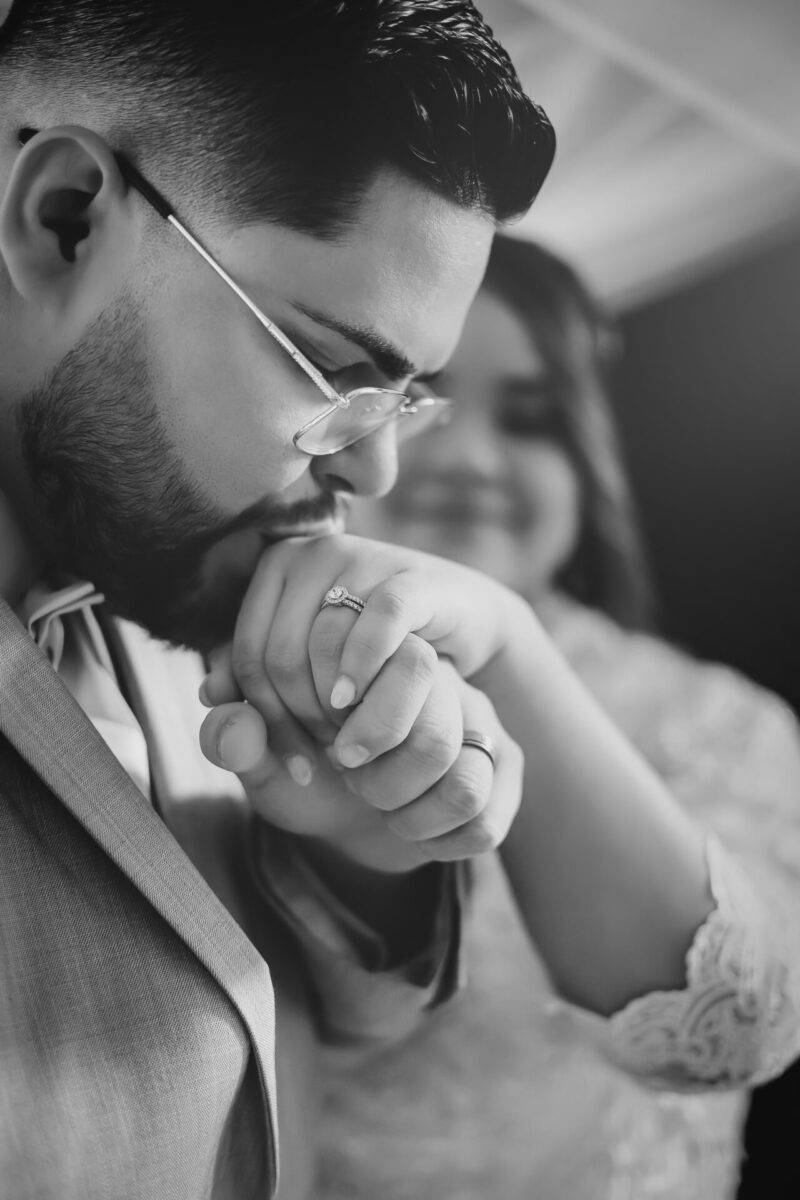 Black and white portrait of a couple, with the man gently kissing the woman's hand, showcasing a close-up of an engagement ring. Captured by JCenteno Photography in Tampa, FL, illustrating romantic and intimate moments.