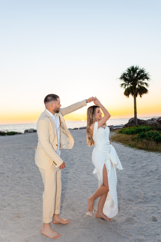 B+G_WeddingPortrait-46 Bride and groom holding hands and dancing on a sandy beach at Tarpon Springs Florida next to a palm tree.