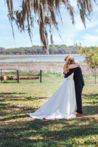 Candid wedding portrait of a couple hugging after their ceremony at an outdoor Florida venue, featuring a scenic lake view and Spanish moss.