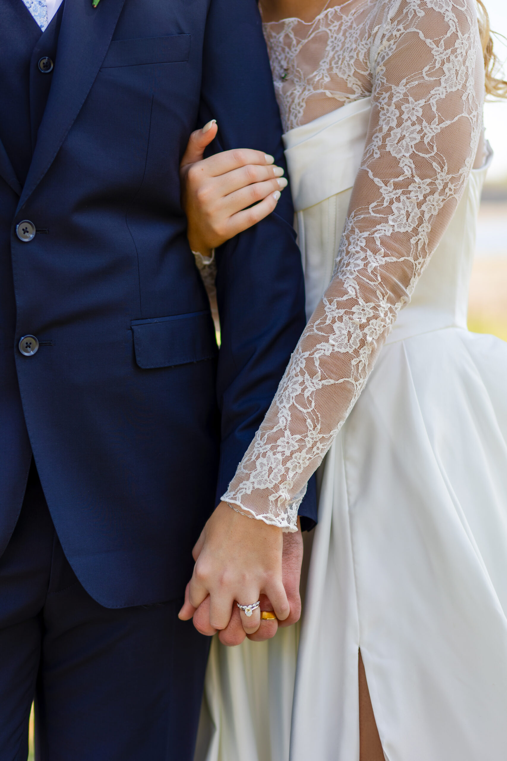 Romantic wedding couple portrait in Florida, showing a close-up of the bride's lace sleeves and the groom's navy suit as they hold hands during their sunset session.